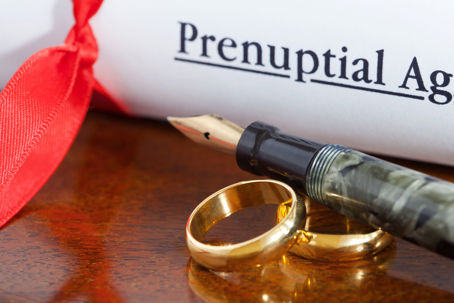 a prenup document, a  pen, and wedding rings