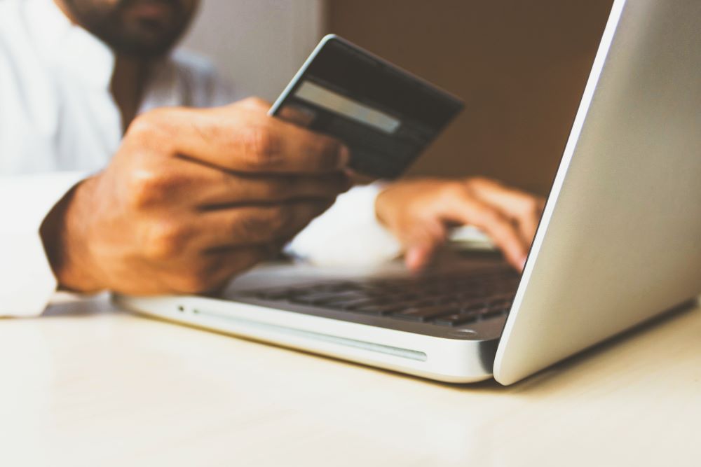 Man holding a credit card in one hand and typing on a laptop with the other.